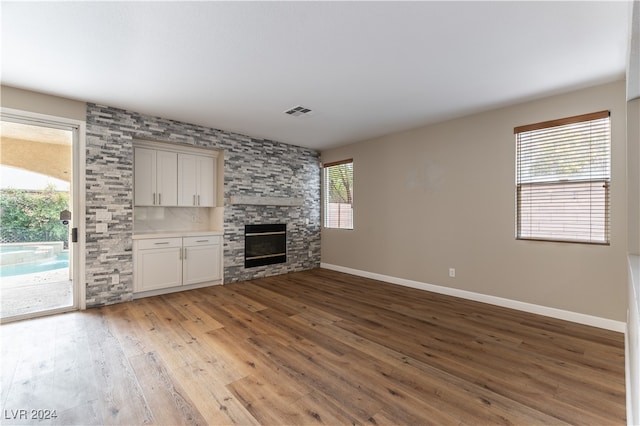 unfurnished living room with a stone fireplace, light wood-type flooring, and plenty of natural light