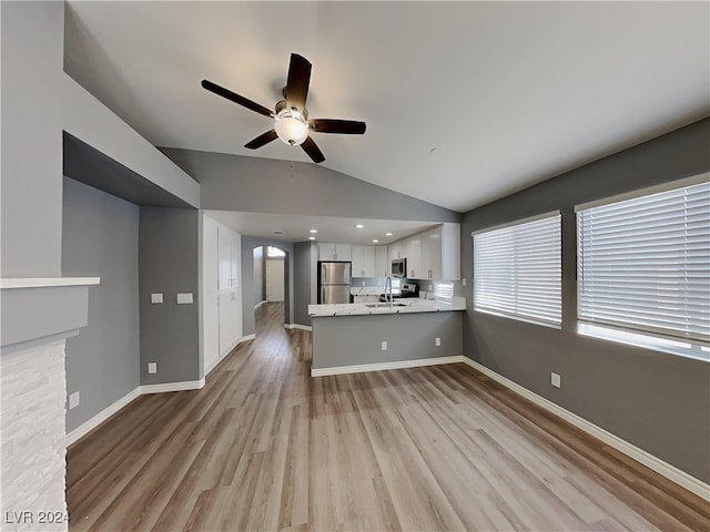 unfurnished living room featuring lofted ceiling, a stone fireplace, sink, light hardwood / wood-style flooring, and ceiling fan