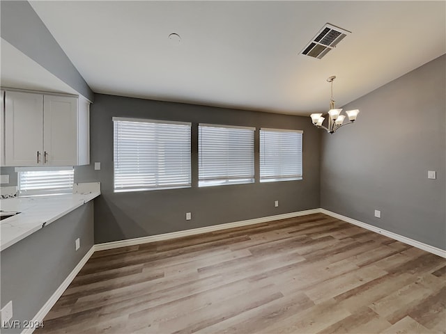 unfurnished dining area featuring a notable chandelier and light wood-type flooring