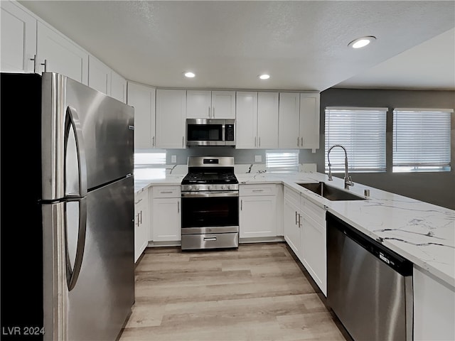 kitchen featuring appliances with stainless steel finishes, light stone counters, sink, light hardwood / wood-style flooring, and white cabinetry