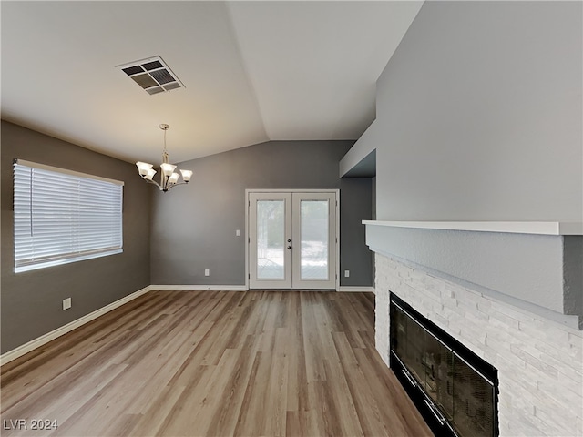 unfurnished living room with french doors, an inviting chandelier, light hardwood / wood-style floors, vaulted ceiling, and a fireplace