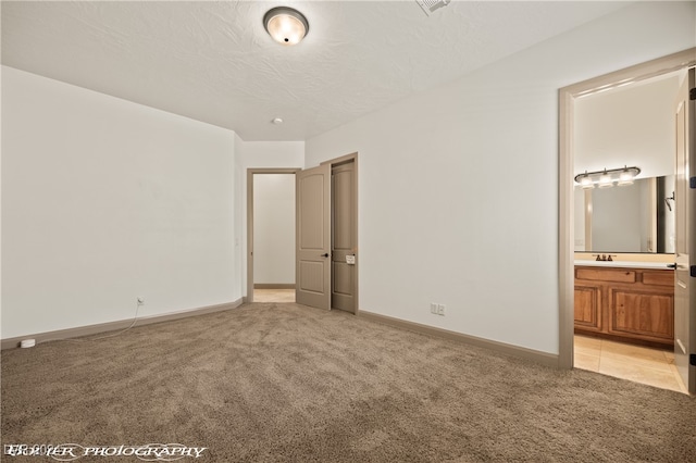 unfurnished bedroom featuring connected bathroom, light carpet, and a textured ceiling