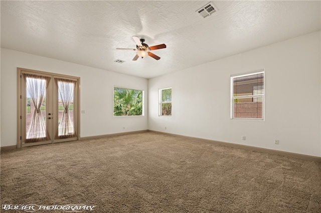 empty room featuring carpet, ceiling fan, a textured ceiling, and plenty of natural light