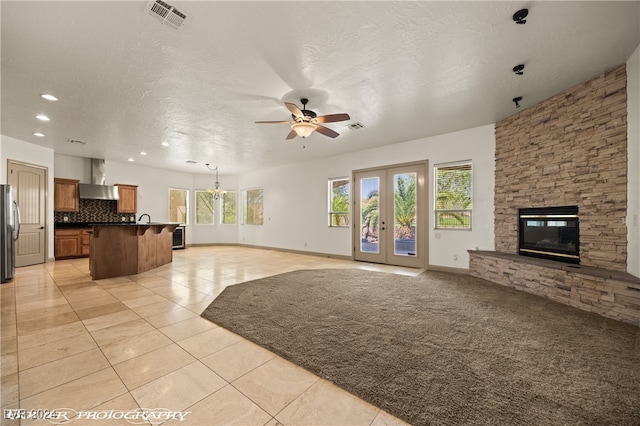 unfurnished living room featuring light tile patterned floors, ceiling fan, a textured ceiling, a stone fireplace, and french doors