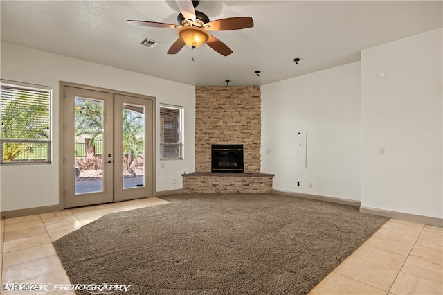 unfurnished living room with french doors, ceiling fan, a fireplace, and light tile patterned floors