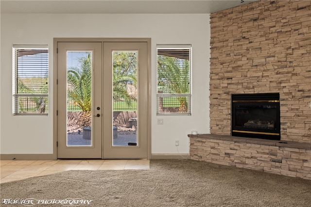 entryway with a stone fireplace, french doors, and light colored carpet