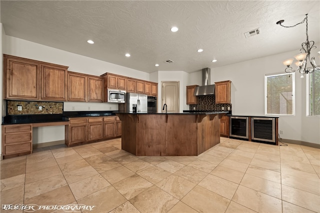 kitchen featuring stainless steel appliances, wall chimney exhaust hood, an island with sink, and tasteful backsplash