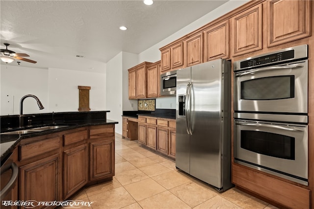 kitchen featuring appliances with stainless steel finishes, a textured ceiling, sink, and dark stone counters