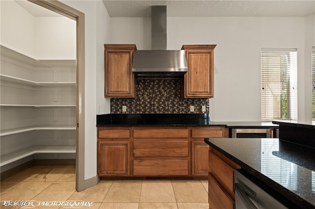 kitchen with light tile patterned flooring, wall chimney exhaust hood, dark stone counters, stainless steel dishwasher, and decorative backsplash