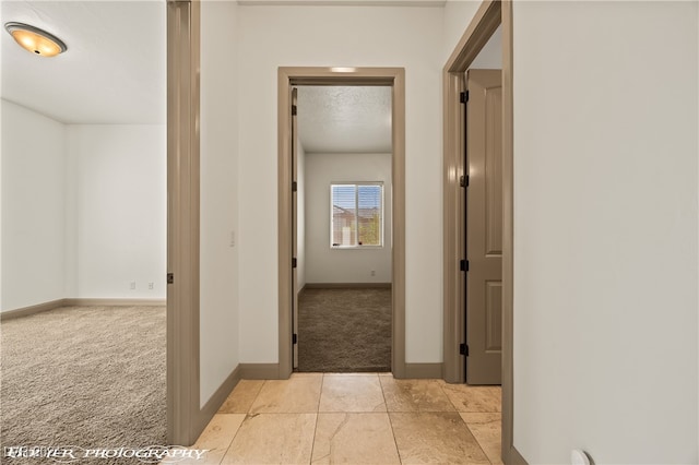 corridor with light carpet and a textured ceiling