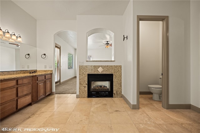 bathroom with vanity, a multi sided fireplace, toilet, and ceiling fan