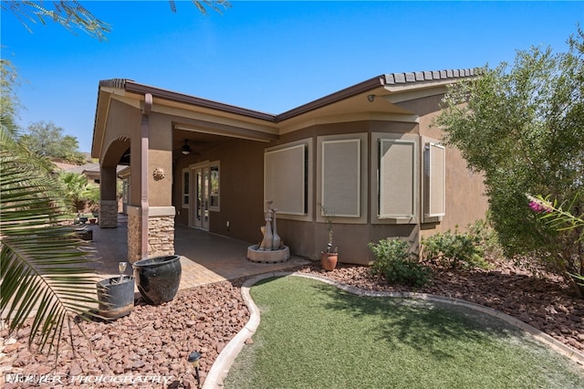 view of side of property with a patio, a lawn, and ceiling fan