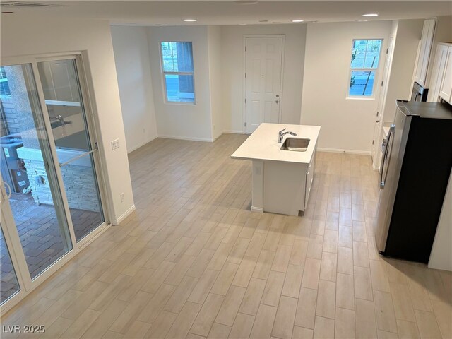 kitchen with stainless steel fridge, white cabinetry, a kitchen island with sink, and sink