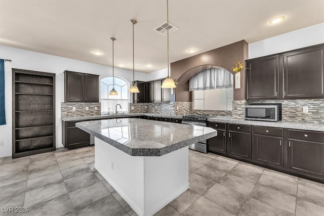 kitchen with tasteful backsplash, dark brown cabinets, appliances with stainless steel finishes, pendant lighting, and a center island