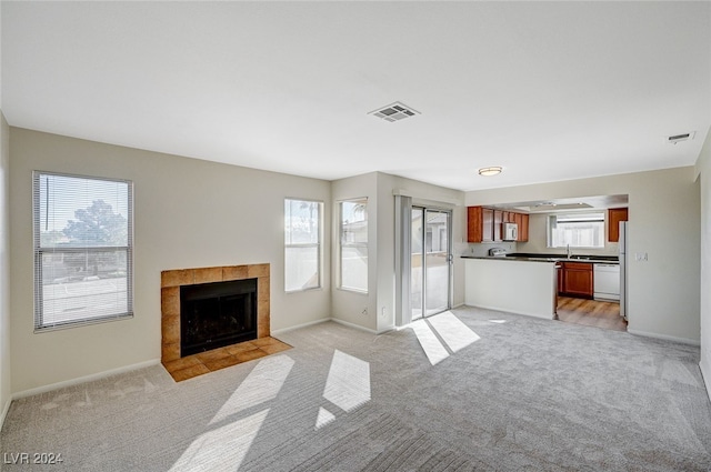 unfurnished living room with light carpet, a healthy amount of sunlight, sink, and a tile fireplace