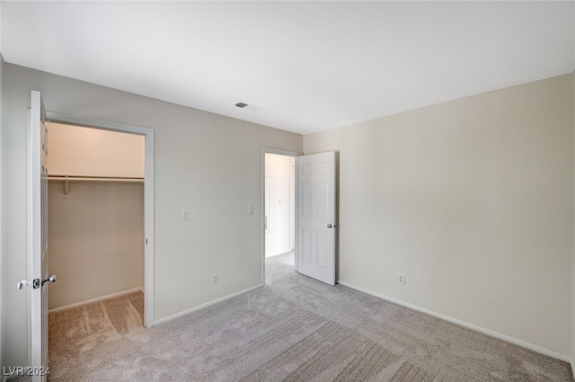 unfurnished bedroom with a spacious closet, light carpet, and a closet