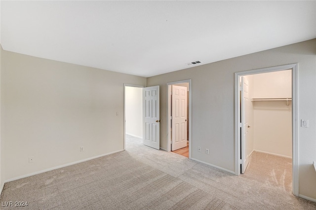 unfurnished bedroom with a walk in closet, a closet, and light colored carpet