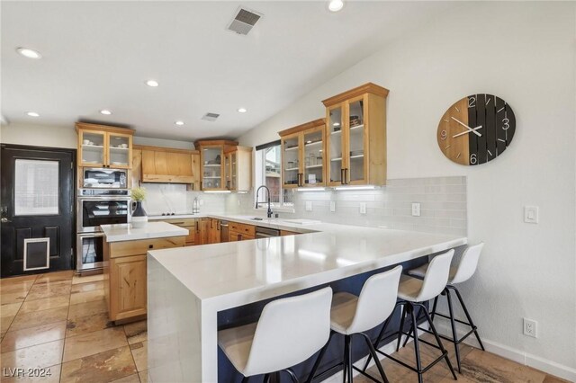 kitchen with backsplash, sink, a kitchen bar, kitchen peninsula, and stainless steel appliances