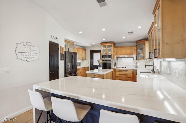 kitchen featuring kitchen peninsula, appliances with stainless steel finishes, decorative backsplash, and a kitchen breakfast bar