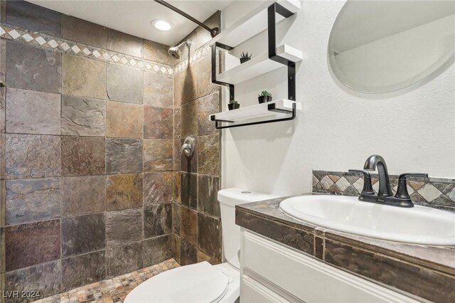 bathroom with tiled shower, vanity, and toilet