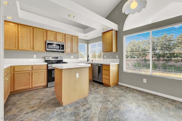 kitchen with ceiling fan, appliances with stainless steel finishes, a kitchen island, tile counters, and sink