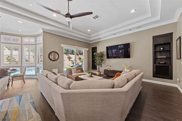 living room featuring crown molding, a raised ceiling, dark hardwood / wood-style floors, and ceiling fan