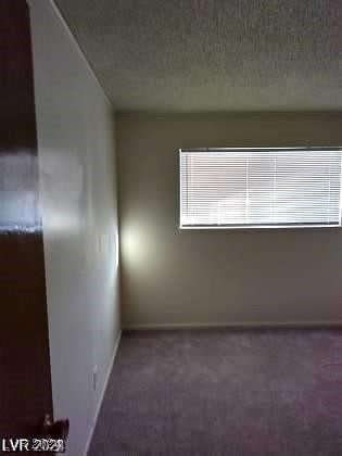 spare room featuring a textured ceiling and dark colored carpet