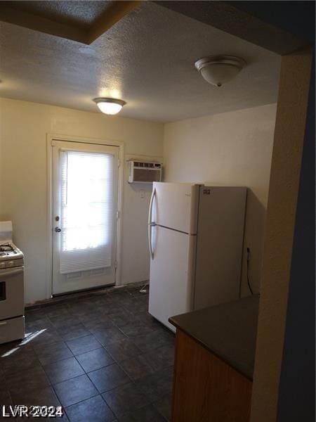1929 Evelyn Ave, Henderson, NV 89011 - kitchen featuring white appliances, a wall unit AC, a textured ceiling, and dark tile patterned flooring