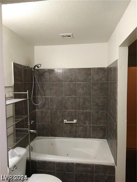 bathroom featuring toilet, a textured ceiling, and tiled shower / bath