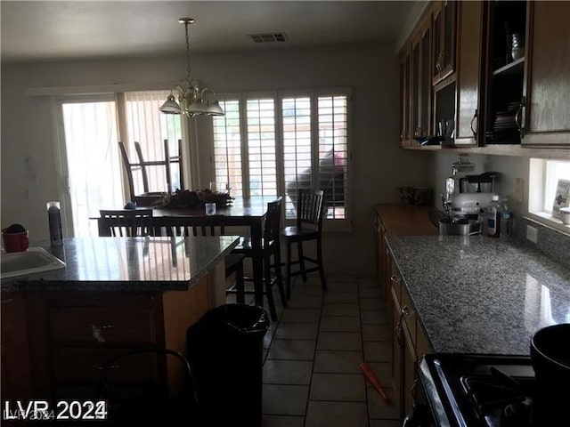 kitchen with dark tile patterned flooring, dark stone countertops, decorative light fixtures, and plenty of natural light