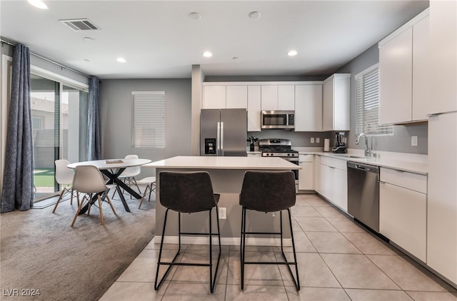 kitchen featuring white cabinets, a kitchen island, appliances with stainless steel finishes, light colored carpet, and sink