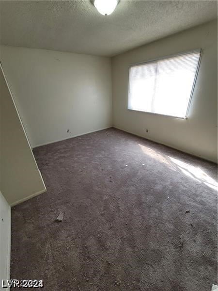 unfurnished room featuring a textured ceiling and dark colored carpet