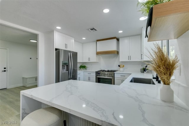 kitchen with premium range hood, kitchen peninsula, white cabinetry, and appliances with stainless steel finishes