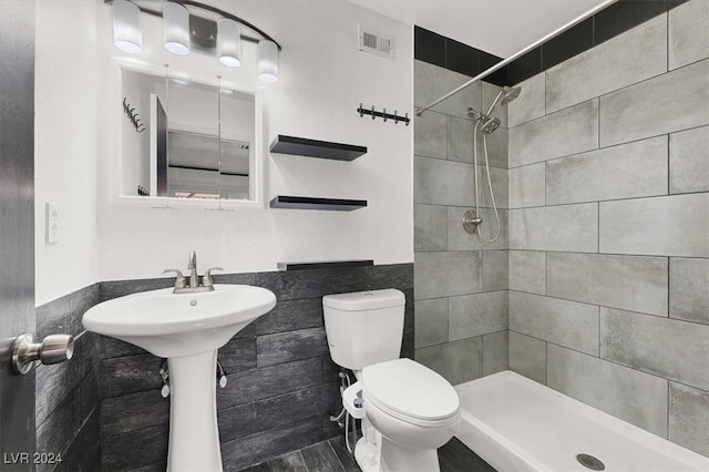 bathroom with tiled shower, tile walls, and toilet