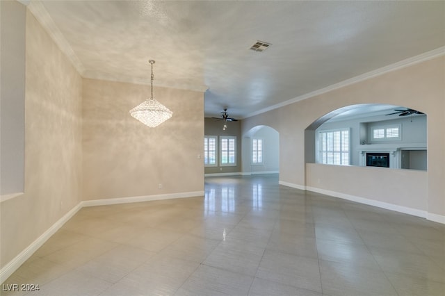 tiled spare room featuring ornamental molding, ceiling fan with notable chandelier, and plenty of natural light