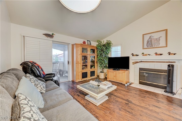 living room featuring vaulted ceiling, wood-type flooring, a tile fireplace, and plenty of natural light