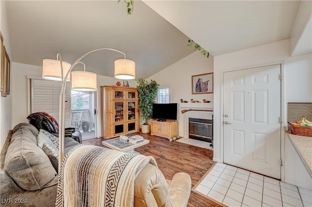 living room with a tile fireplace, lofted ceiling, and light wood-style floors