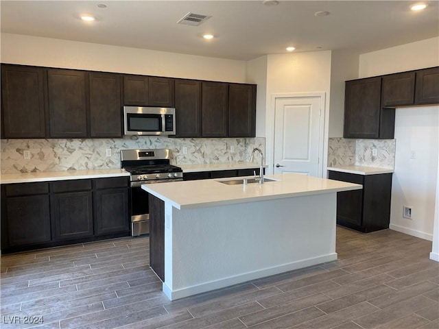 kitchen featuring sink, dark brown cabinets, a center island with sink, stainless steel appliances, and decorative backsplash