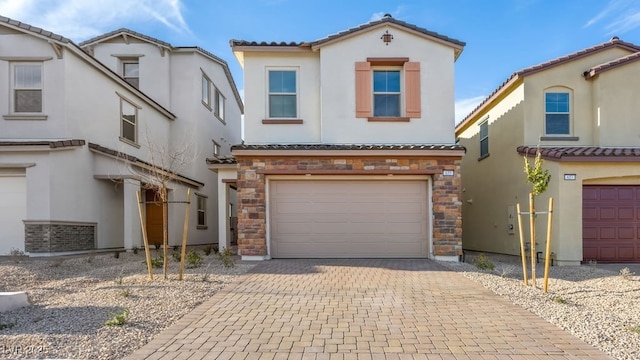 mediterranean / spanish-style home featuring stone siding, decorative driveway, a tiled roof, and a garage