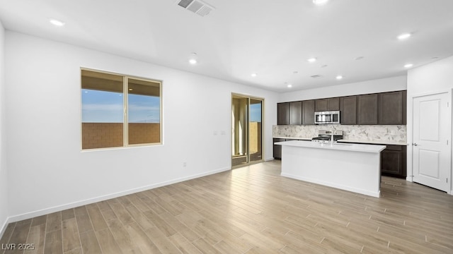 kitchen featuring tasteful backsplash, light countertops, visible vents, appliances with stainless steel finishes, and an island with sink