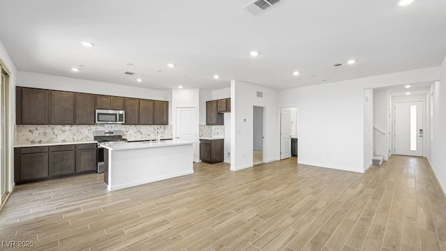 kitchen with a kitchen island with sink, stainless steel appliances, a sink, visible vents, and light countertops