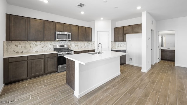 kitchen featuring wood finish floors, stainless steel appliances, light countertops, a kitchen island with sink, and a sink