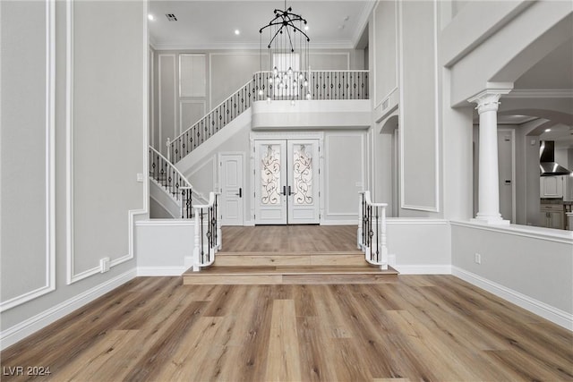 foyer featuring french doors, an inviting chandelier, a towering ceiling, hardwood / wood-style flooring, and ornamental molding