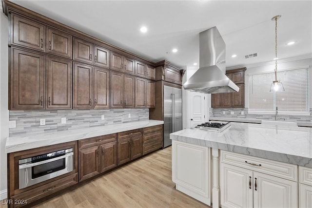 kitchen featuring tasteful backsplash, ventilation hood, stainless steel appliances, decorative light fixtures, and light hardwood / wood-style floors