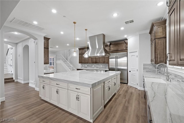 kitchen with hardwood / wood-style floors, built in fridge, light stone countertops, range hood, and tasteful backsplash