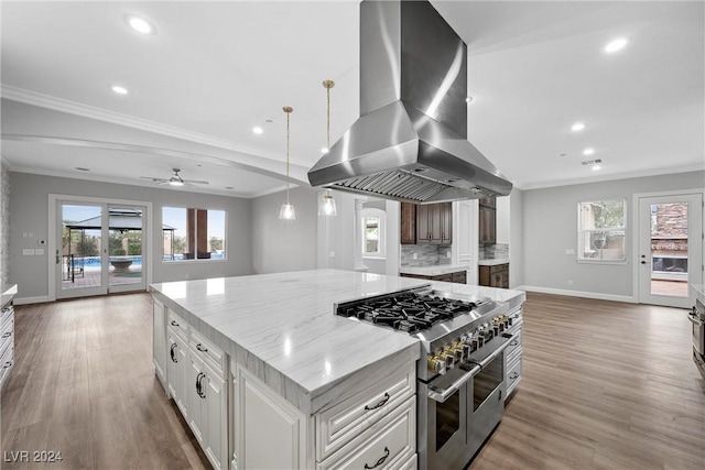 kitchen with island range hood, double oven range, white cabinetry, and a healthy amount of sunlight