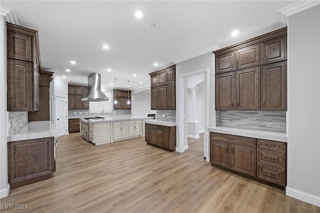 kitchen with light wood-type flooring, tasteful backsplash, ornamental molding, and wall chimney range hood