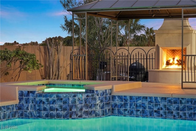 pool at dusk featuring an in ground hot tub