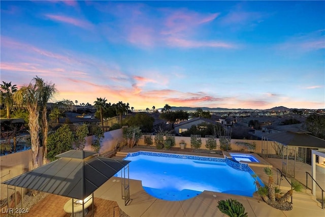 pool at dusk with an in ground hot tub and a patio