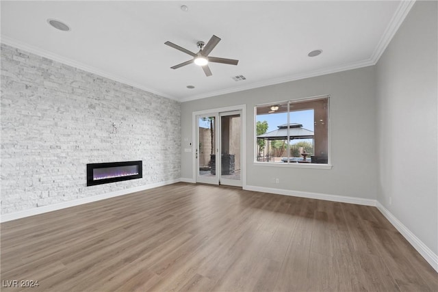 unfurnished living room with hardwood / wood-style floors, ceiling fan, a stone fireplace, and ornamental molding